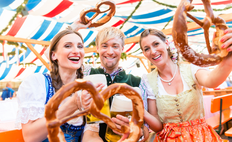 Three people at Wurstfest in New Braunfels holding up a large pretzel